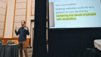 A picture of me! I'm gesticulating mid-speech in a conference ballroom next to a screen showing the slide "What is web accessibility? Making websites work for any person on any device by centering the needs of people with disabilities."