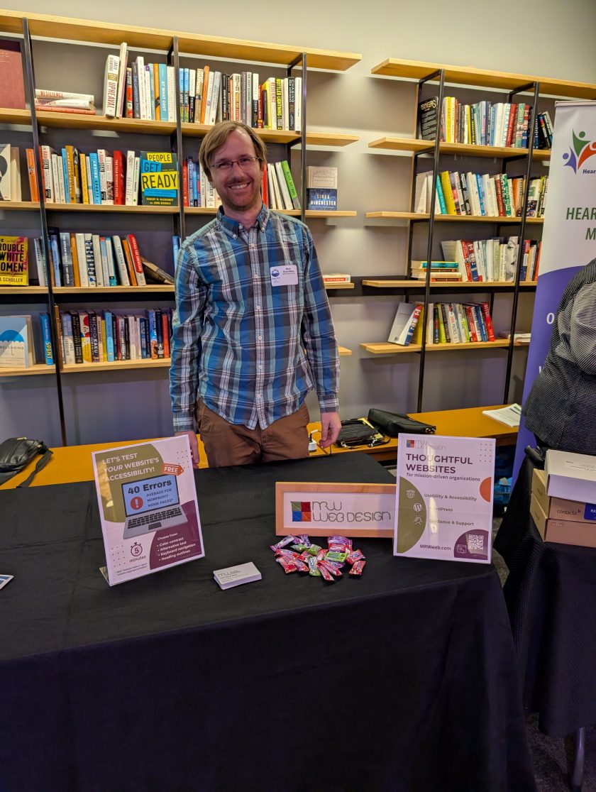 Me standing at my sponsor table with 3 signs, business cards, and candy